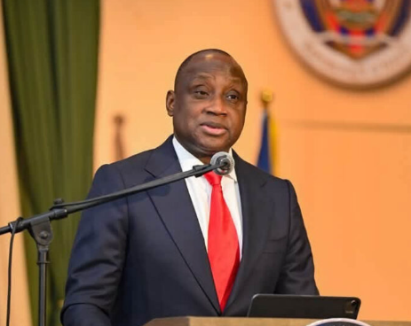 Portrait officiel du Ministre de la Défense à un pupitre, devant le drapeau haïtien.